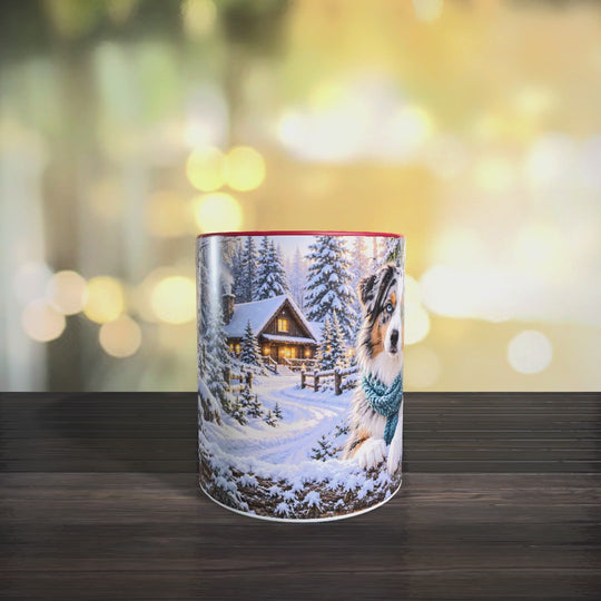 Video der Australian-Shepherd-Tasse mit winterlichem Hundemotiv, verschneiter Holzhütte sowie roter Innenseite und rotem Henkel.